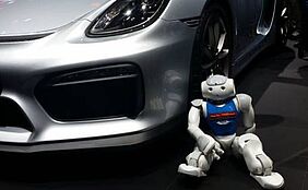 NAO-Roboter vor einem silbernen Wagen