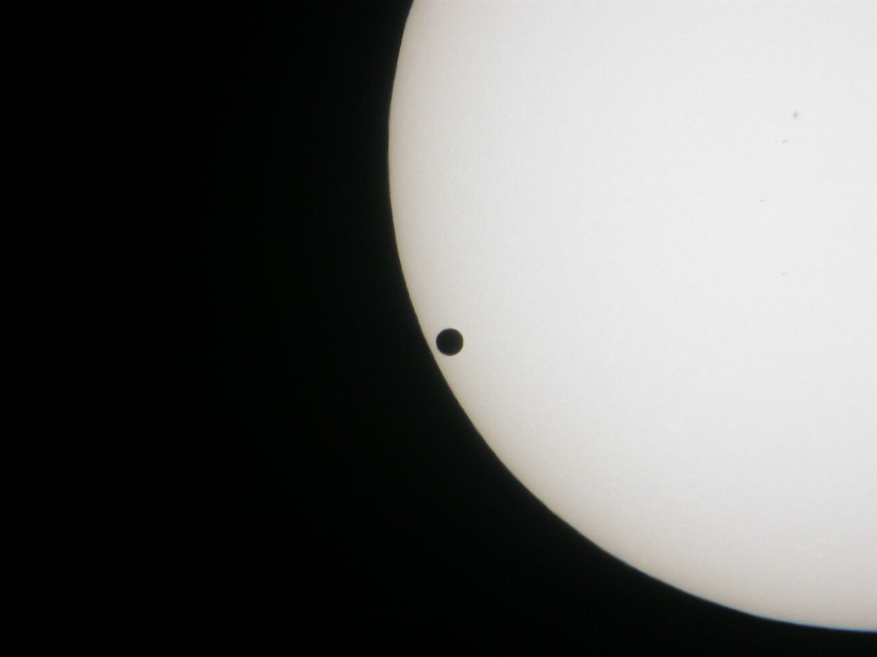 Zu sehen ist das untere linke Viertel der Sonne im Weiß-Licht, vor ihr ist die Venus als schwarzer Punkt zu sehen. 