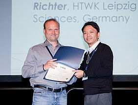 Prof. Hendrik Richter erhält von Konferenzleiter Prof. Yew-Soon Ong die Urkunde für seinen Konferenzbeitrag.